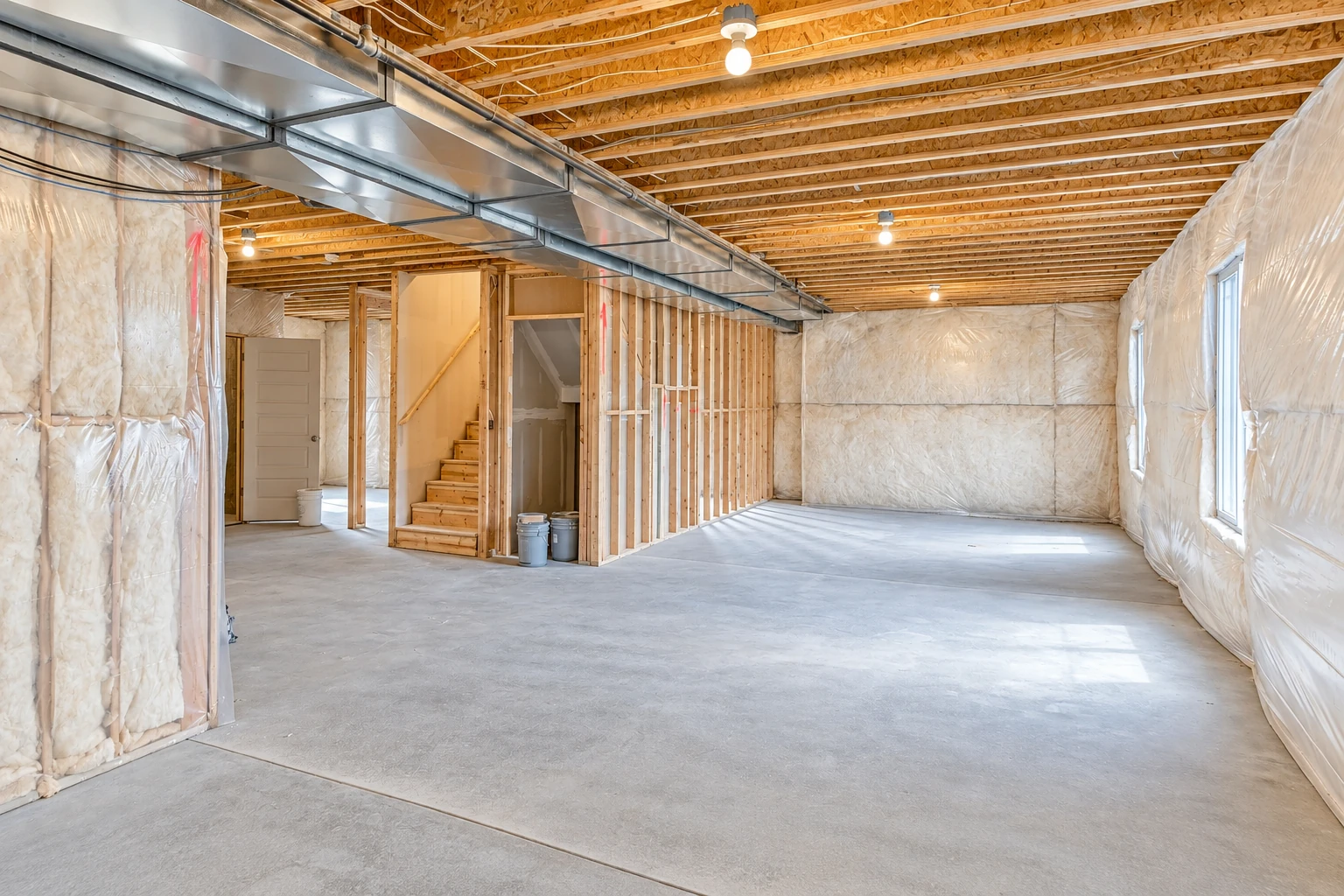 Unfinished basement with insulation covering the walls, exposed ceiling joists, metal ductwork, and a concrete floor.