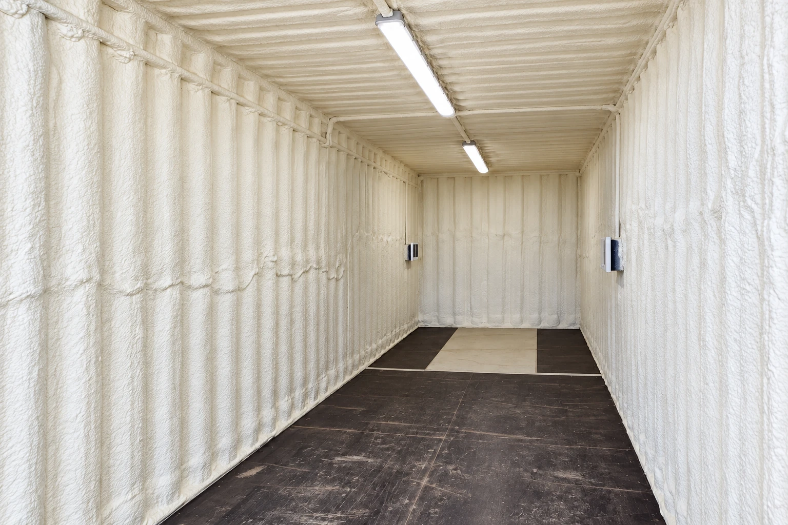 Narrow room with white closed-cell foam insulation coating the walls and ceiling above a dark tiled floor.