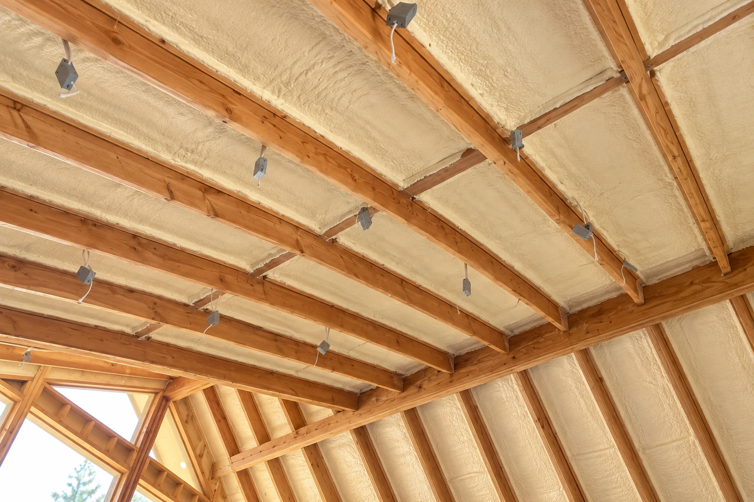 Open-cell spray foam fills the spaces between exposed wooden roof rafters and wall framing.