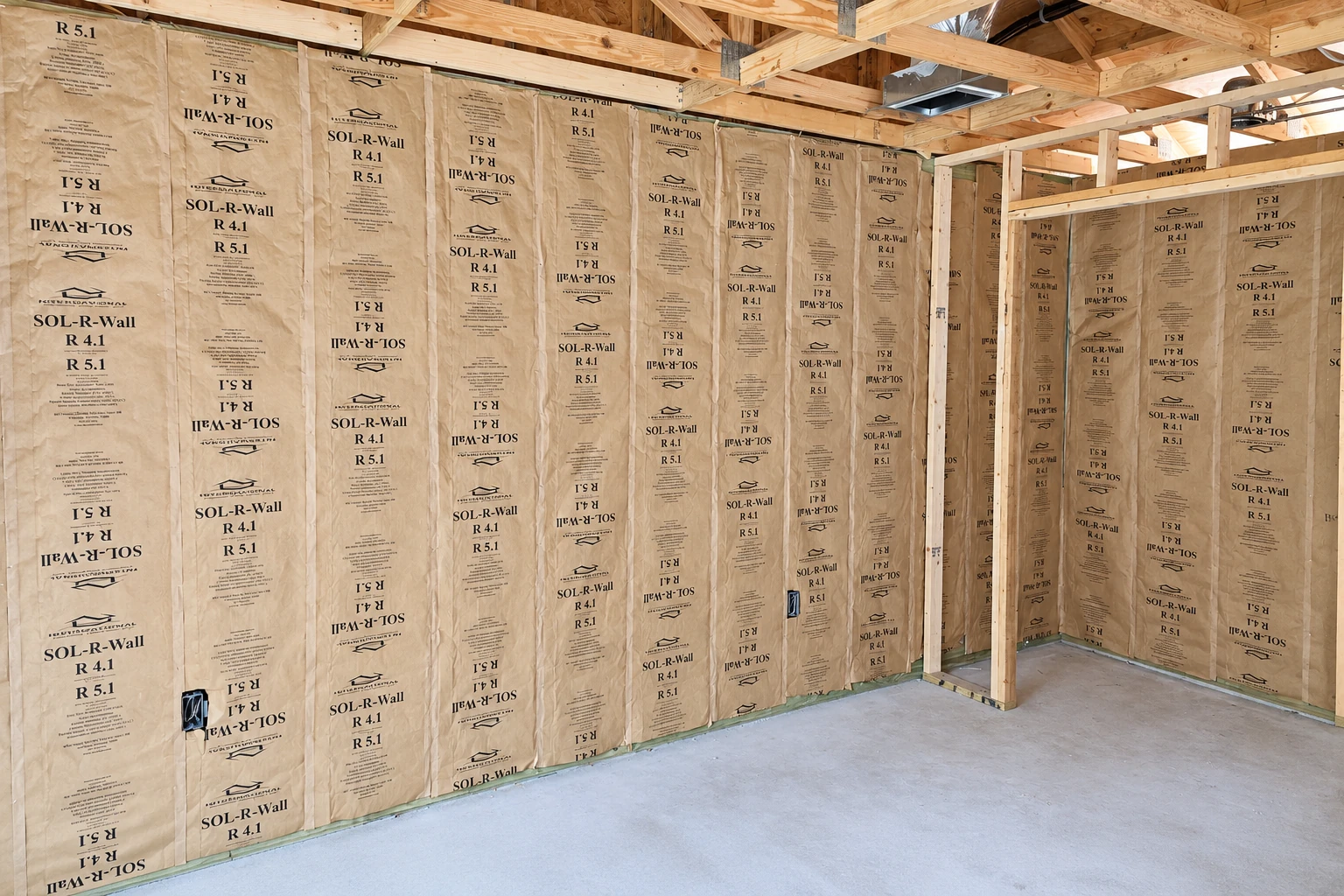 Wall insulation with kraft-faced fiberglass batts fitted between exposed wooden studs in an unfinished room.